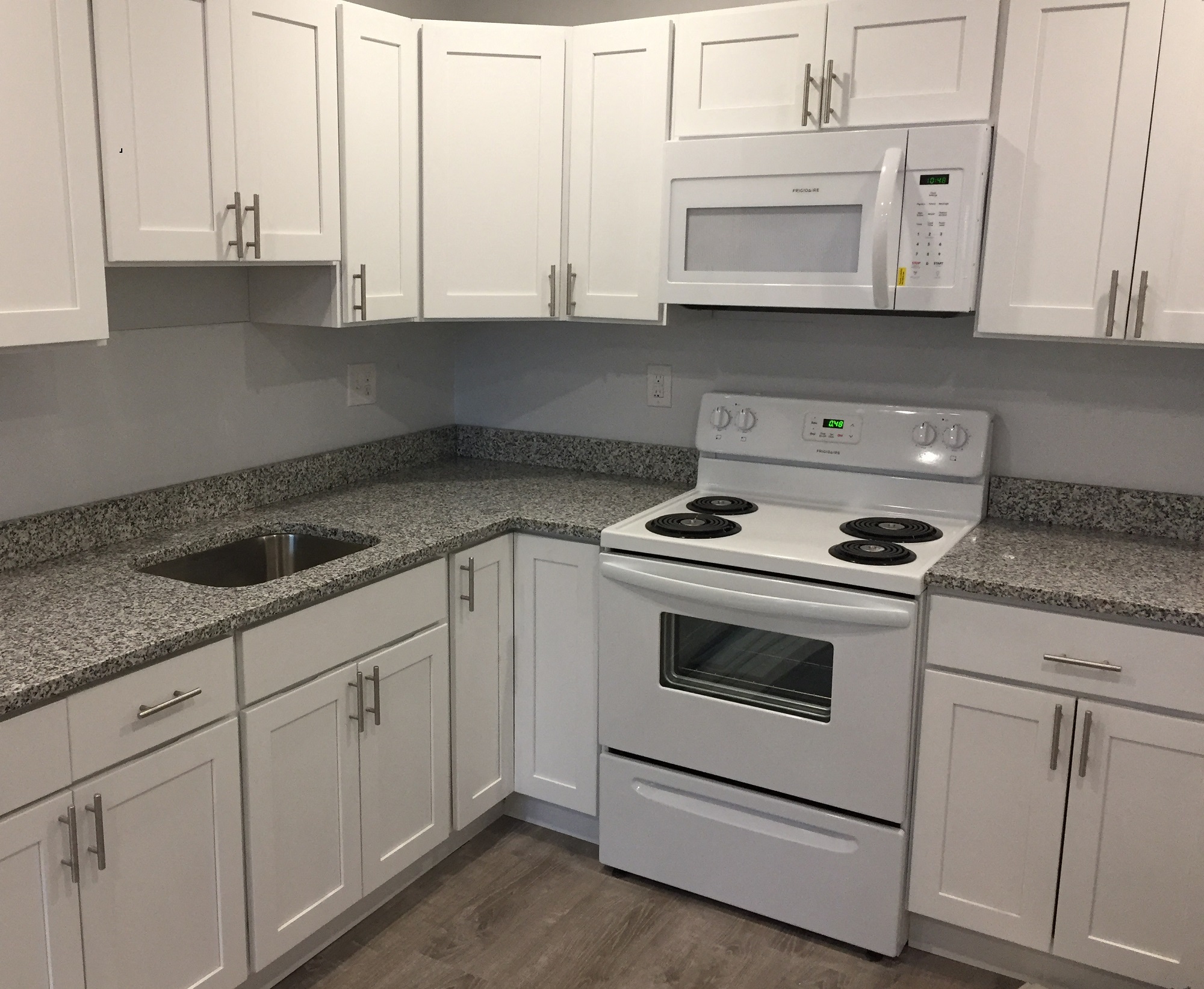 Renovated kitchen with granite counters, white cabinets and white appliances